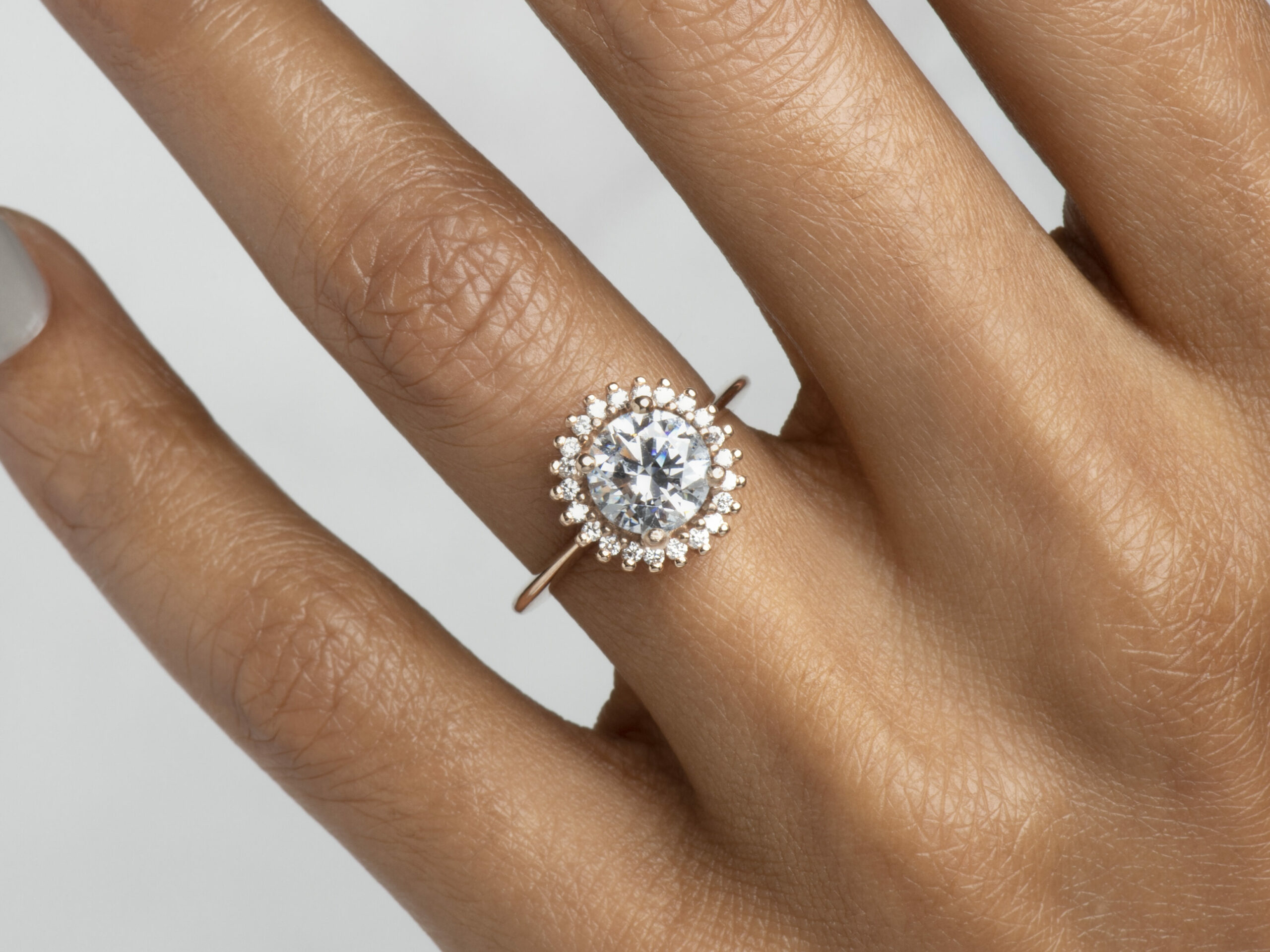 Close-up of a hand showcasing a classic halo-style ring with a brilliant diamond center stone encircled by a shimmering diamond halo.