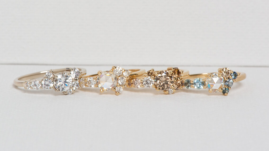 A row of cluster diamond rings, each featuring a variety of colored diamonds and other gemstones.