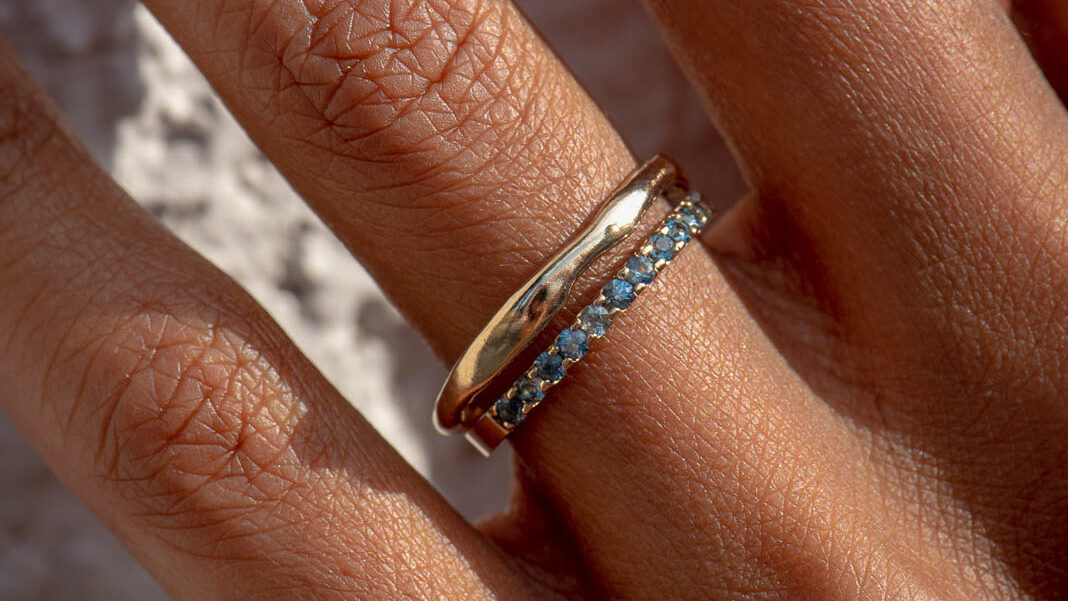 Close up of hand wearing a thin band and a band of sapphires on the ring finger