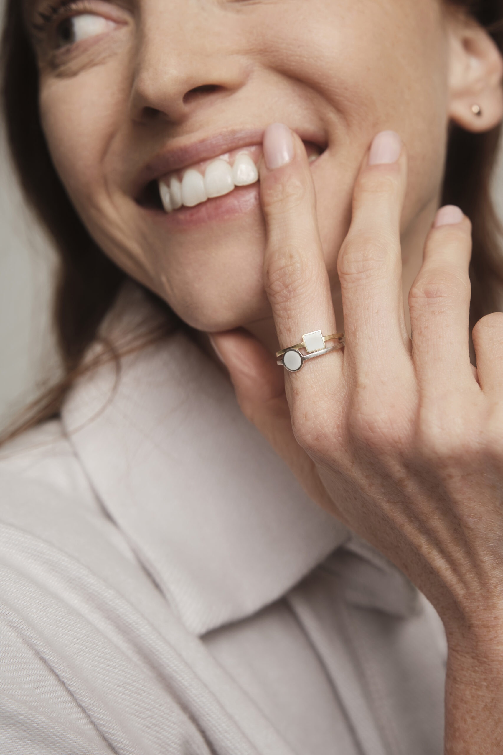 woman with hand gracefully placed on cheek, showcasing a stack of rings on her pointer finger. they are enamel rings